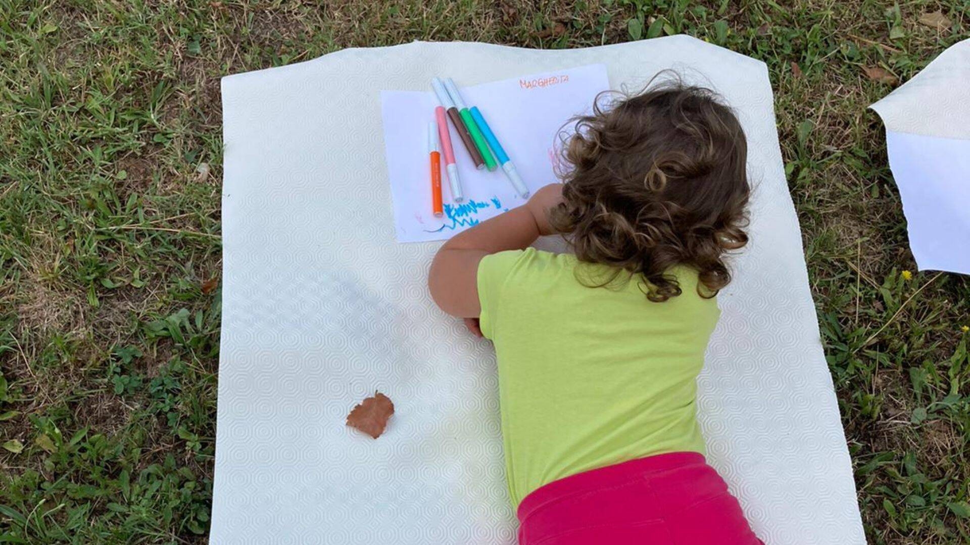Foto bambina che disegna stesa su un prato