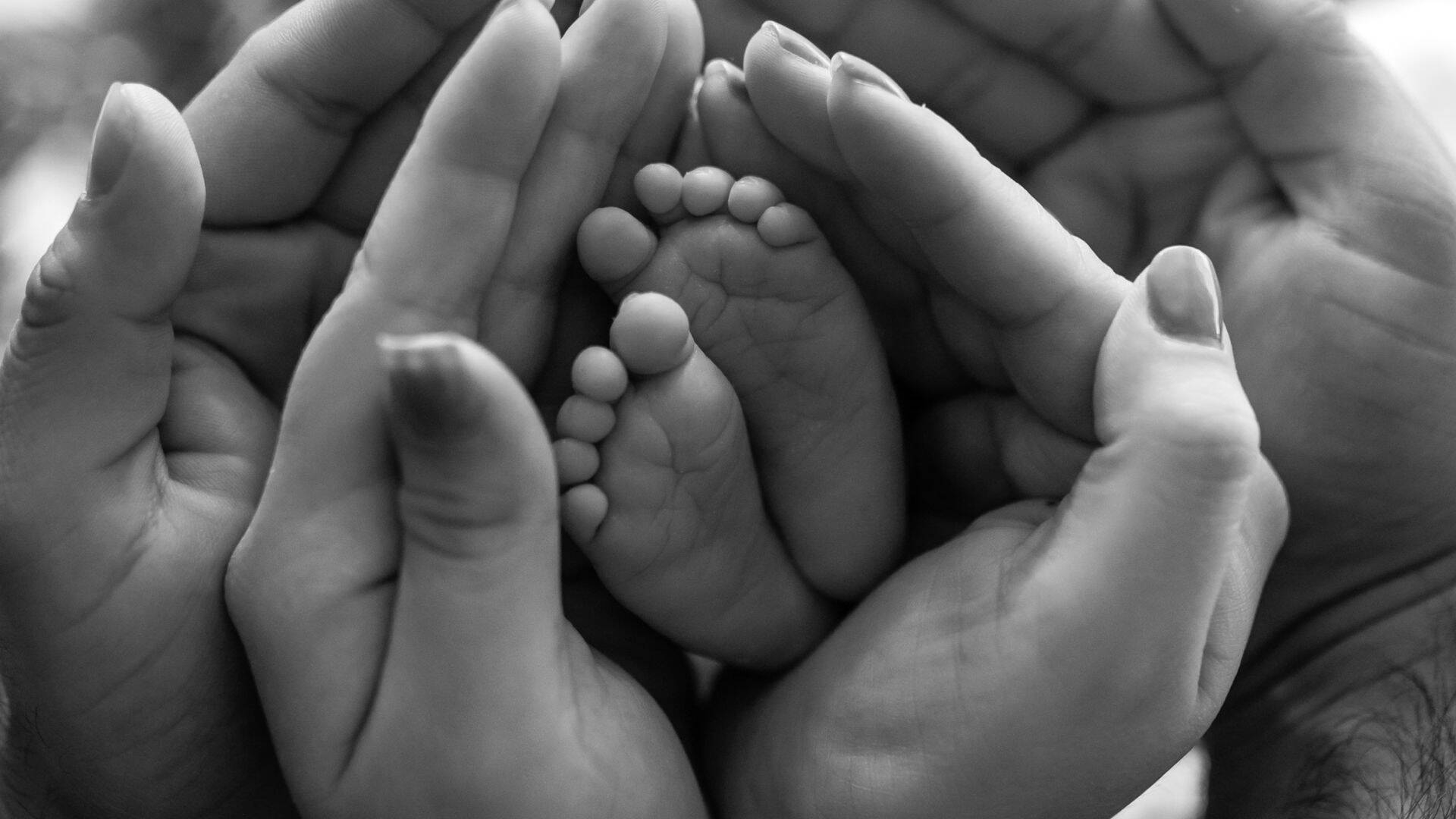 mani che abbracciano i piedini di un neonato 